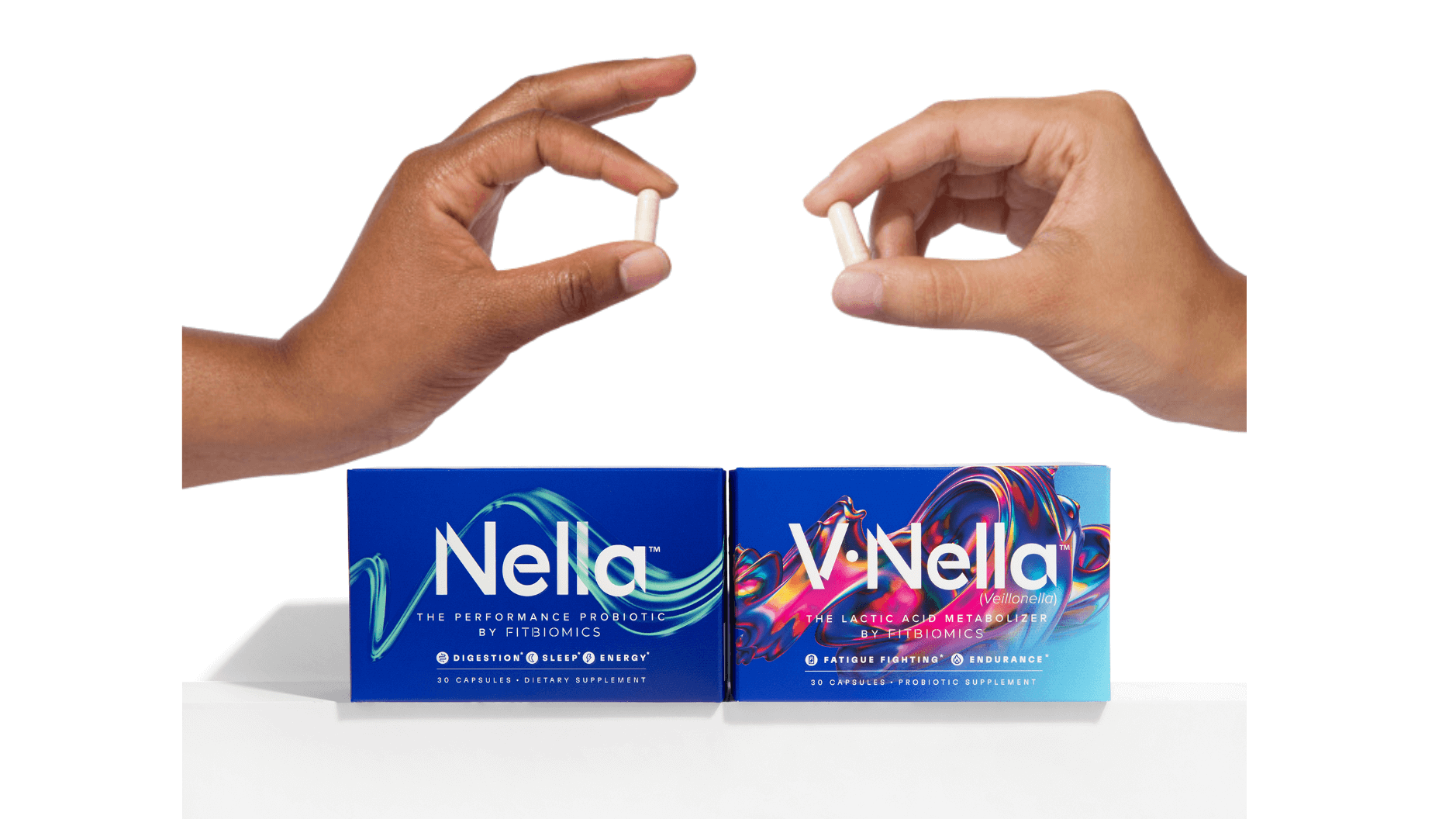two hand each holding a white capsule above a box of nella and v•nella