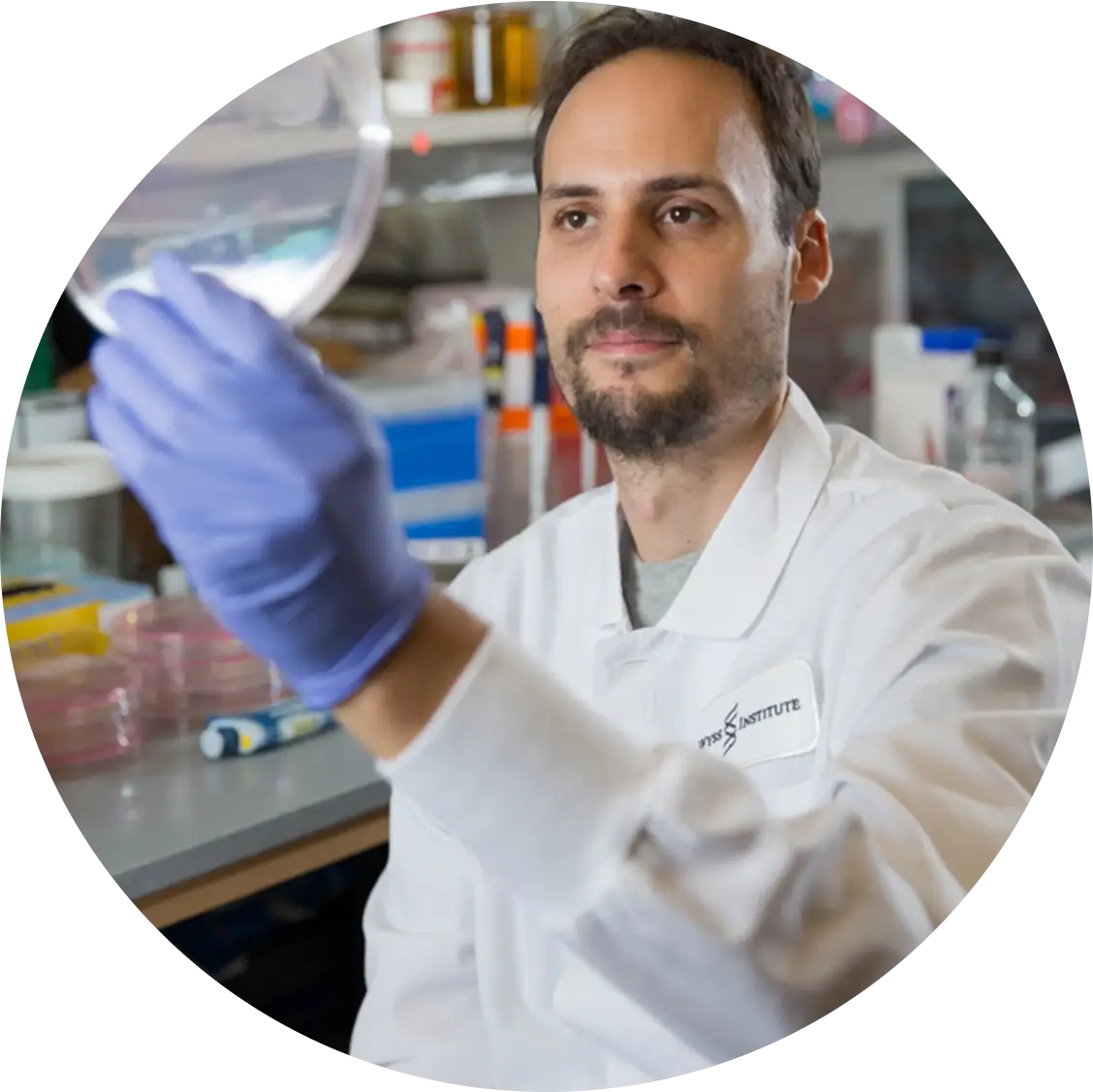 jonathan scheiman in a lab coat holding up a petri dish to examine